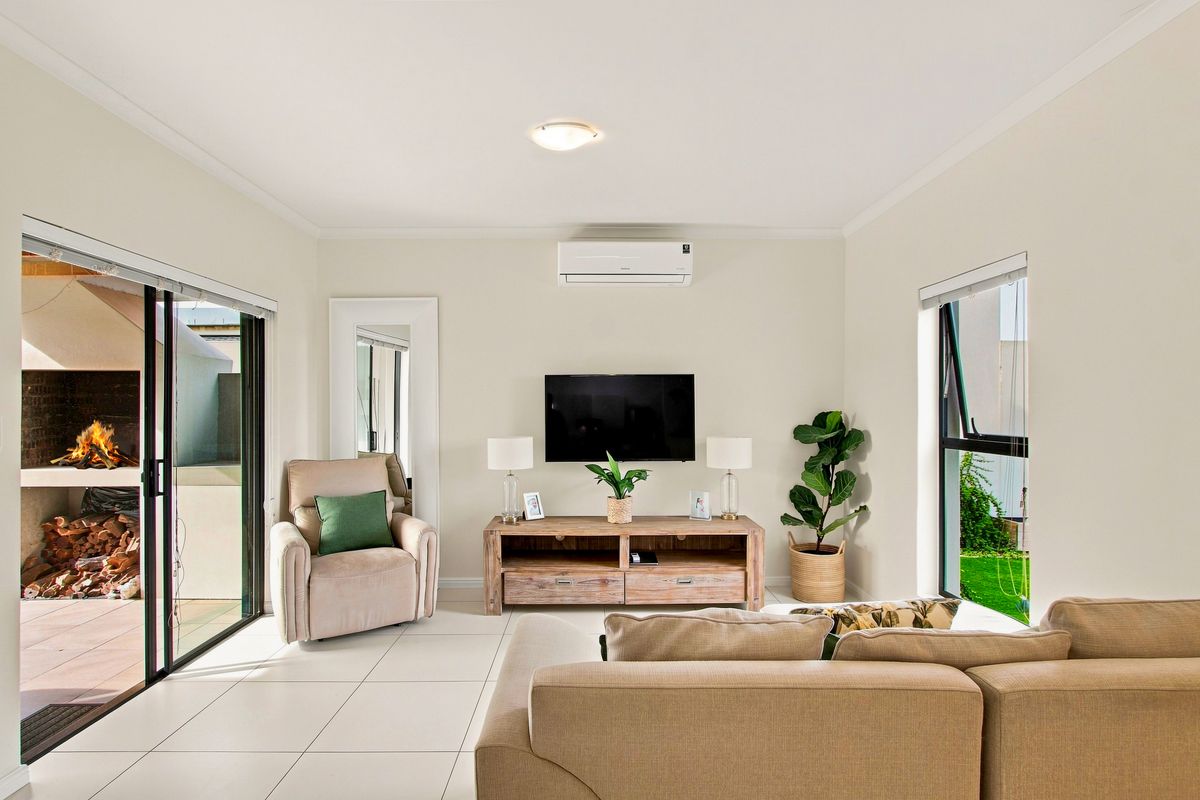 A bright and well-maintained living room featuring tiled flooring, a split-system air conditioner, and large sliding glass doors leading to an outdoor patio area.