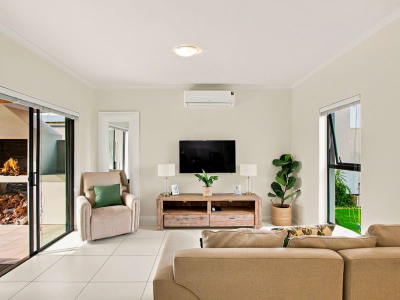A bright and well-maintained living room featuring tiled flooring, a split-system air conditioner, and large sliding glass doors leading to an outdoor patio area.