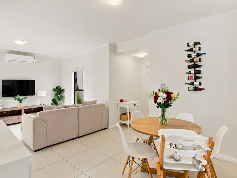 Bright open-plan living and dining area featuring neutral tiled flooring, coving, and a wall-mounted split-system air conditioner.