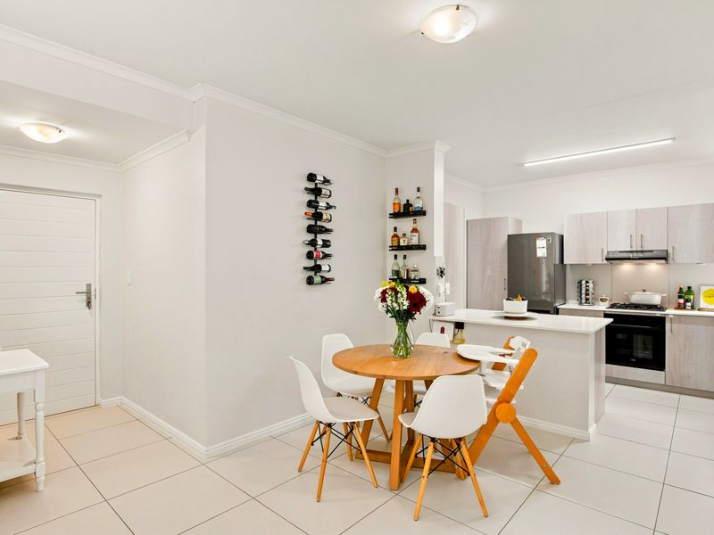 Modern open-plan kitchen and dining area featuring neutral cabinetry, stone countertops, integrated appliances, and clean tiled flooring throughout.