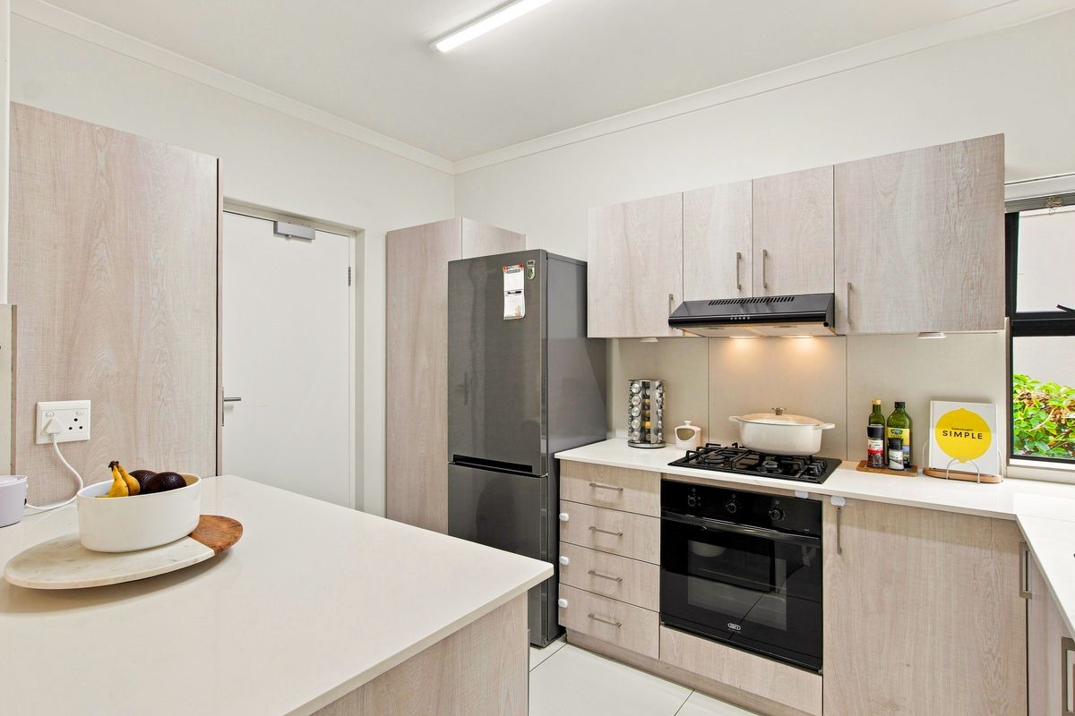 Modern kitchen featuring light wood-grain cabinetry, stone countertops, integrated gas cooktop, built-in oven, and an extractor fan.