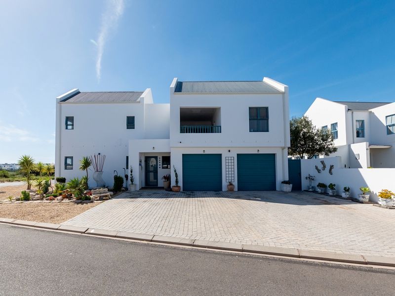 A modern double-story residential property featuring a paved driveway, double garage, and an upper-level balcony under a clear blue sky.
