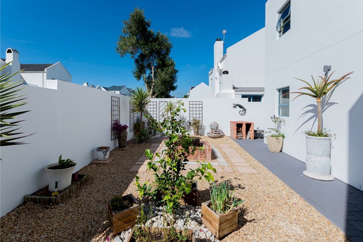 A well-maintained rear courtyard featuring a central brick fire pit, built-in brick braai, gravel landscaping, and a paved walkway along the building exterior.