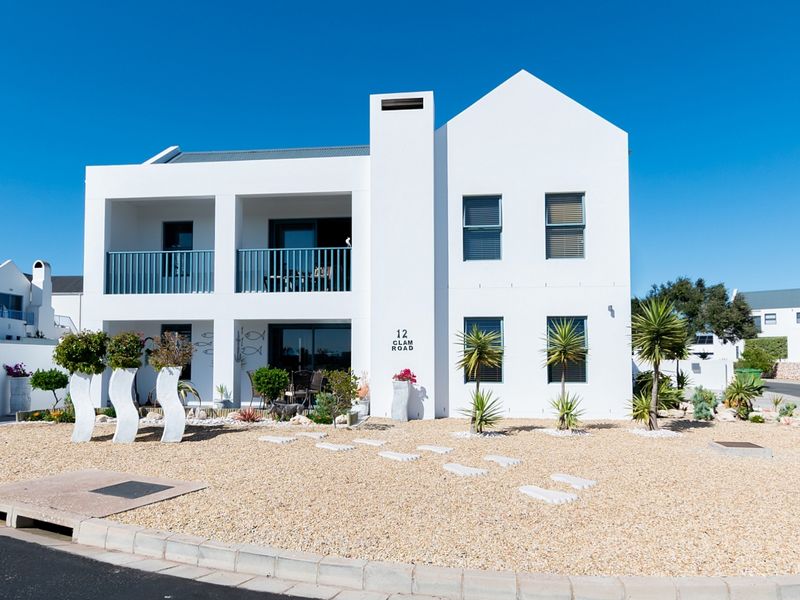 A well-maintained double-storey residential property featuring a clean white facade, upper-level balcony, lower-level patio, and landscaped gravel garden with paved stepping stones.