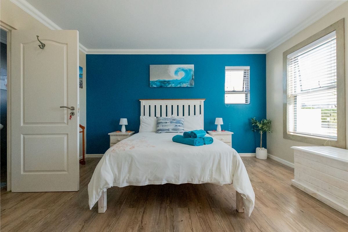 A well-maintained bedroom featuring laminate flooring, a bold blue accent wall, and natural light through venetian blinds.