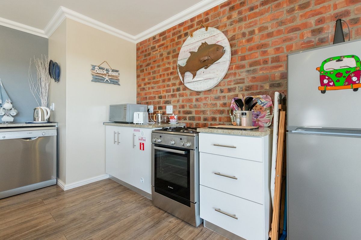 A functional kitchen featuring exposed brick walls, white cabinetry, stone countertops, and a stainless steel gas stove with integrated dishwasher.