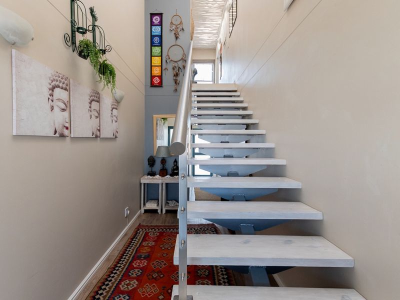 A bright hallway featuring a modern open-tread staircase with a metal handrail and timber steps, leading to an upper level.