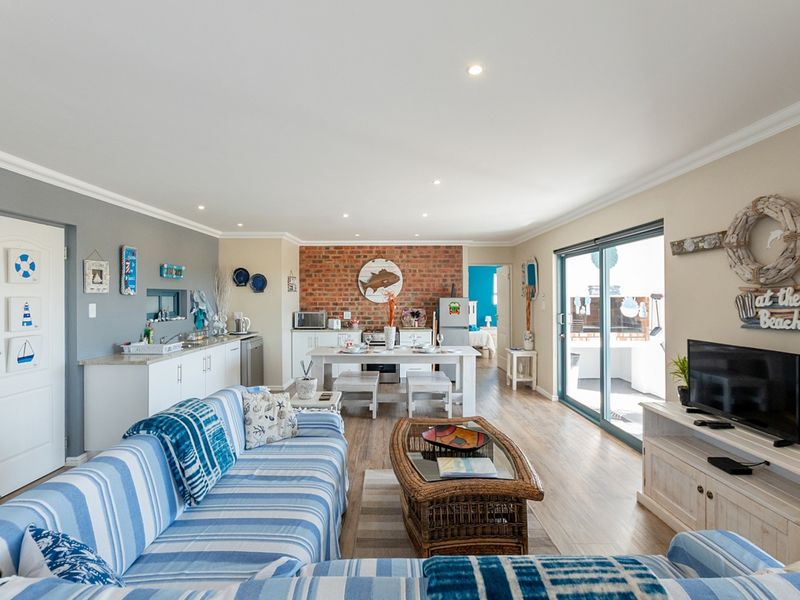 Spacious open-plan living and kitchen area featuring an exposed brick wall, modern laminate flooring, and large sliding doors leading to an outdoor patio.