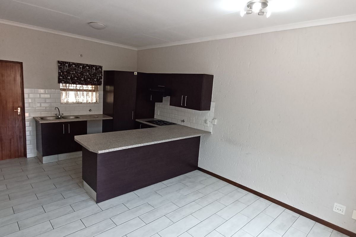 Open plan kitchen featuring dark cabinetry, light laminate countertops, subway tile backsplash, and tiled flooring in a clean, vacant space.