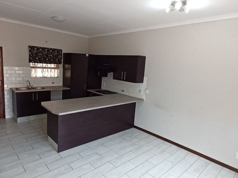 Open plan kitchen featuring dark cabinetry, light laminate countertops, subway tile backsplash, and tiled flooring in a clean, vacant space.