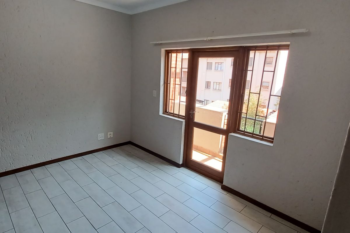 An empty bedroom featuring tiled flooring, a timber door with a security gate, and burglar bars on the window.
