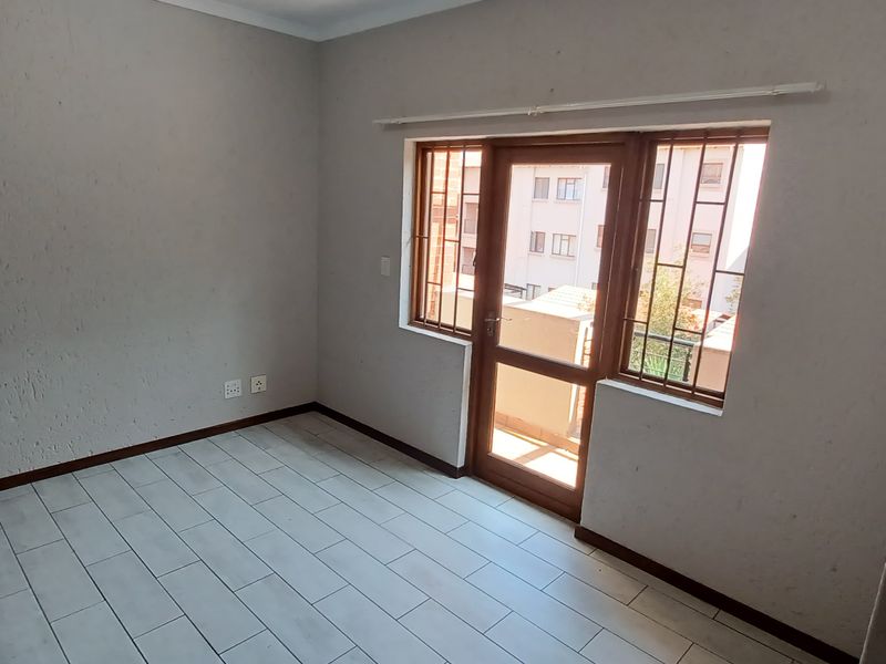 An empty bedroom featuring tiled flooring, a timber door with a security gate, and burglar bars on the window.