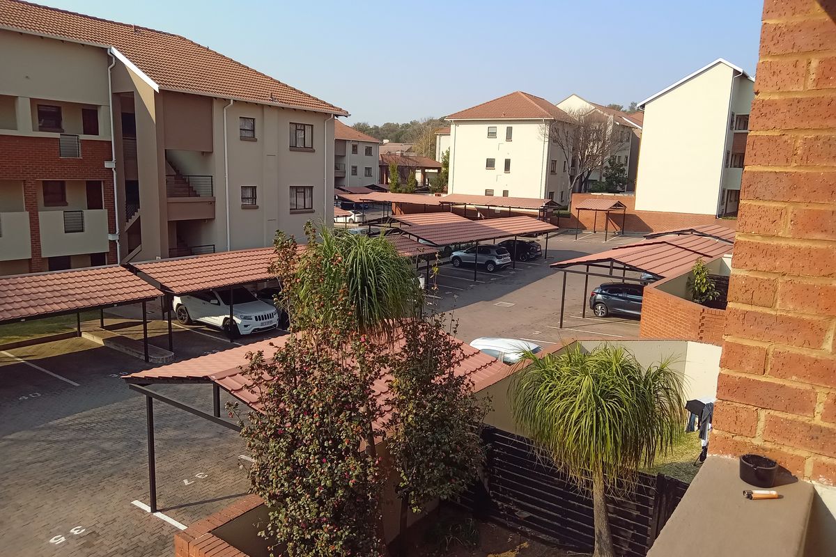 An elevated view of the apartment complex parking area featuring multiple carports, paved driveways, and surrounding residential buildings.