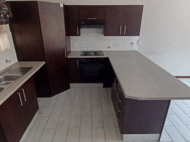 A functional kitchen featuring dark wood cabinetry, laminate countertops, a double basin sink, and built-in cooking appliances with a subway tile backsplash.