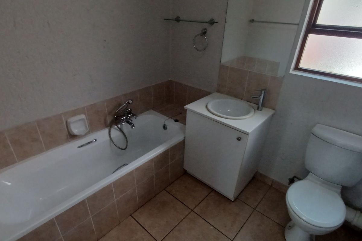 A functional bathroom featuring a bathtub, vanity with basin, and toilet, finished with tiled flooring and splashbacks.