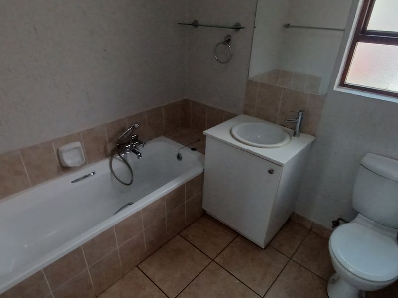 A functional bathroom featuring a bathtub, vanity with basin, and toilet, finished with tiled flooring and splashbacks.