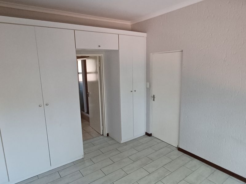 A clean, empty bedroom featuring built-in white cupboards, tiled flooring, and neutral wall finishes, providing a versatile space ready for personalization.
