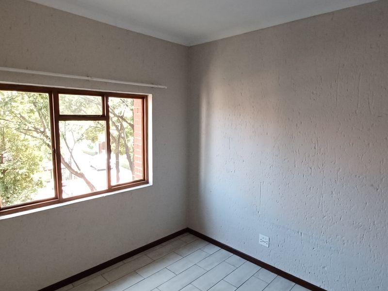 A bright, empty bedroom featuring tiled flooring, textured walls, and a wooden-framed window with an installed curtain rod.