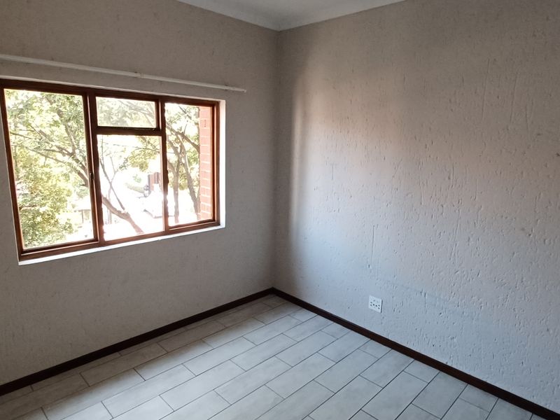 A bright, empty bedroom featuring neutral textured walls, tiled flooring, and a window with a wooden frame.