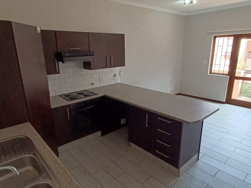 Open plan kitchen and living area featuring dark wood cabinetry, laminate countertops, built-in appliances, and direct access to a balcony through a sliding door.
