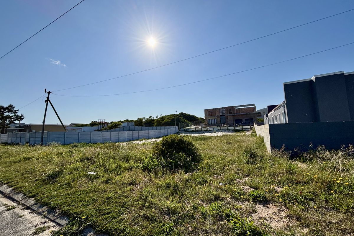 A vacant residential plot featuring perimeter fencing and a utility pole, situated in a developing neighborhood.