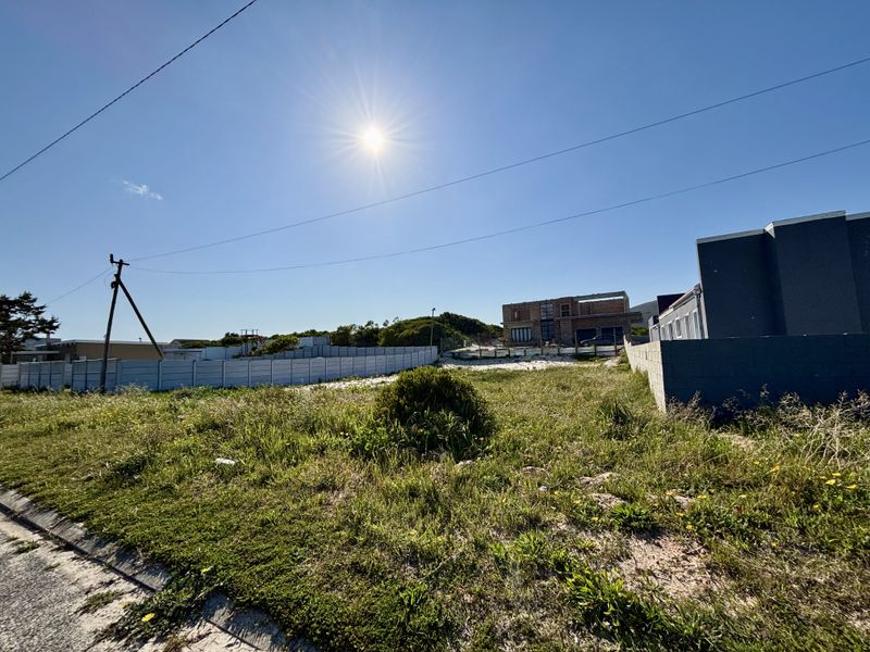 A vacant residential plot featuring perimeter fencing and a utility pole, situated in a developing neighborhood.