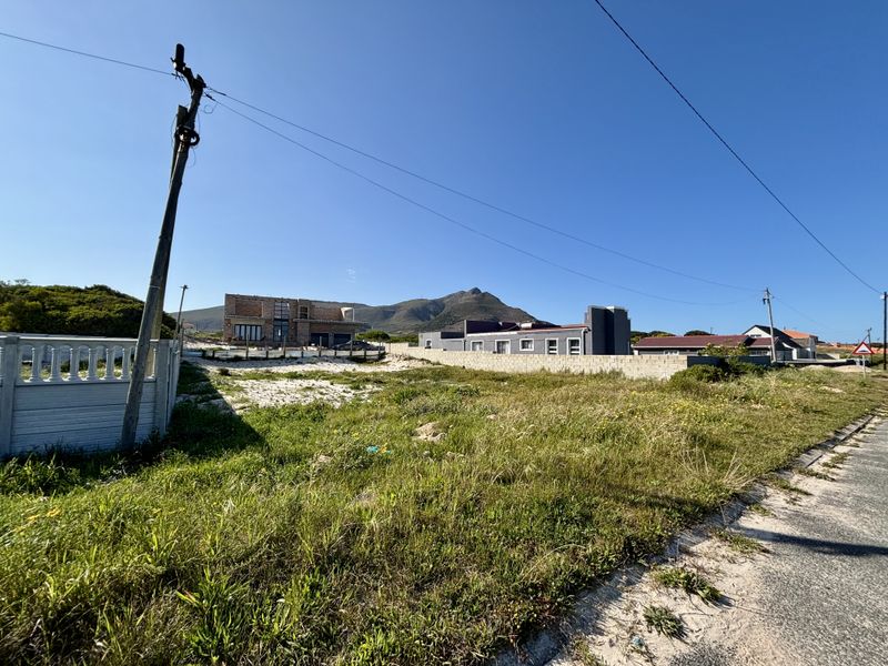 A vacant residential plot featuring a concrete boundary wall, utility pole, and mountain views in a developing neighborhood.
