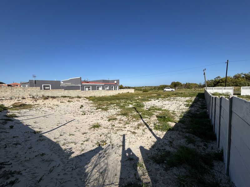 A vacant residential plot featuring sandy ground and enclosed by concrete block and precast boundary walls.