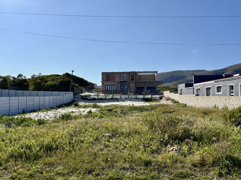 A vacant residential plot featuring sandy ground, enclosed by precast concrete boundary walls, with a partially constructed building visible in the background.