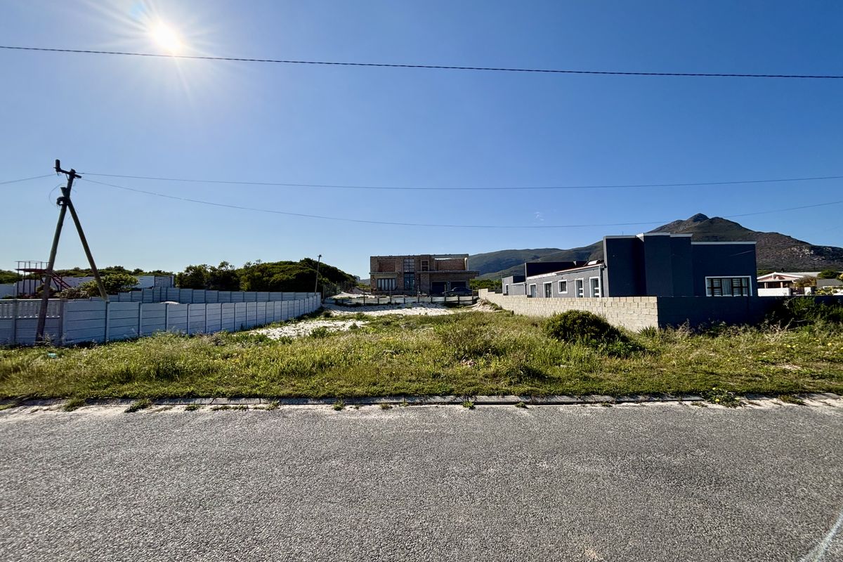 A vacant residential plot featuring a precast concrete boundary wall, situated along an asphalt road with mountain views in the background.