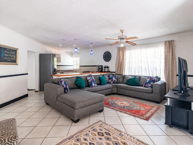 Open-plan living area featuring tiled flooring, a breakfast bar, ceiling fan, and integrated kitchen cabinetry, creating a functional and connected living space.