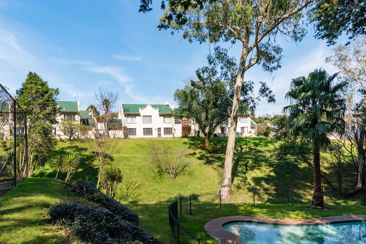 Rear view of the townhouse complex featuring a landscaped garden, mature trees, and a private swimming pool with brick coping.