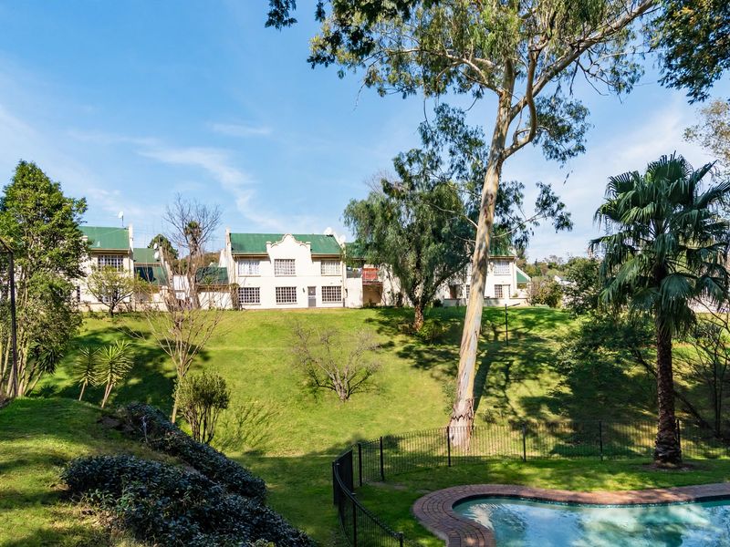 Rear view of the townhouse complex featuring a landscaped garden, mature trees, and a private swimming pool with brick coping.