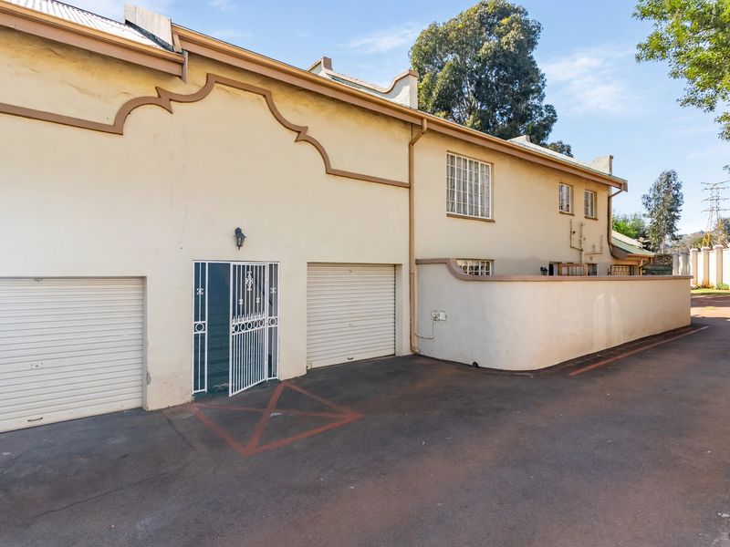 Front exterior view of the townhouse featuring two roller shutter garage doors, a security gate, and a paved driveway area.