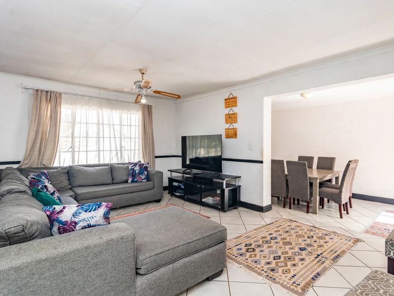 Open-plan living and dining area featuring tiled flooring, a ceiling fan, and large windows providing natural light.