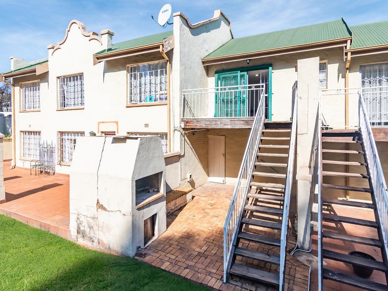 Rear exterior view of a townhouse featuring a paved patio, built-in braai, and external metal staircase leading to an upper-level balcony.