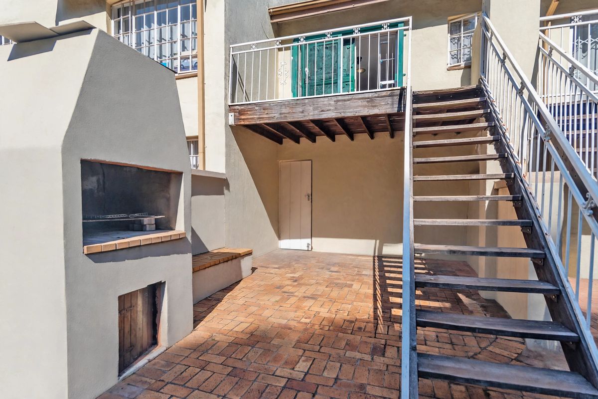 Rear courtyard area featuring a built-in braai, brick paving, and an external staircase leading to an elevated wooden deck.