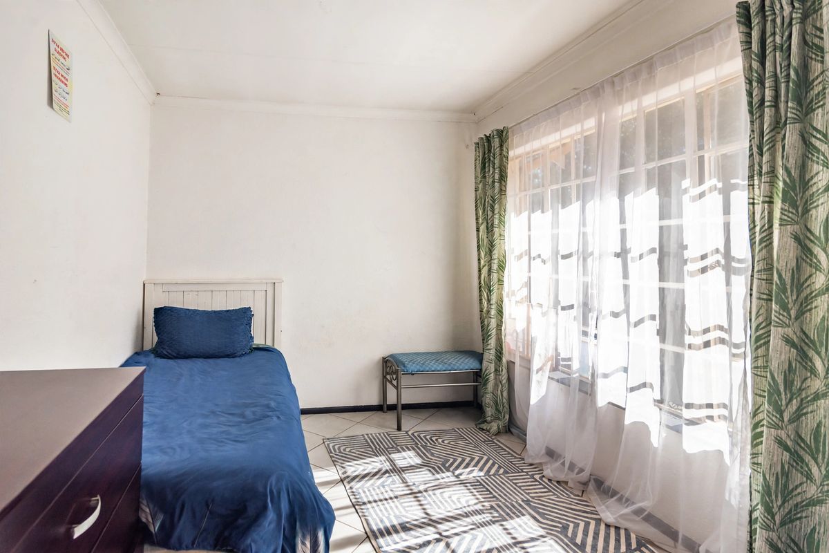 A bedroom featuring tiled flooring, a large window with security bars, and coved ceilings, offering a functional space with potential for cosmetic updates.