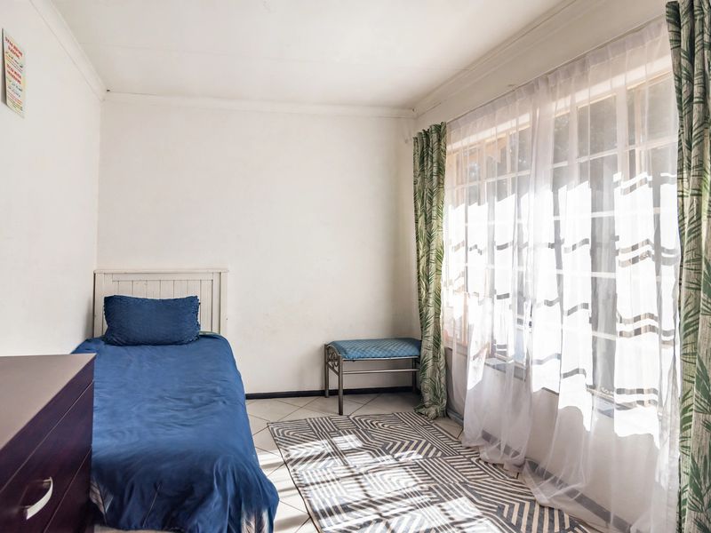 A bedroom featuring tiled flooring, a large window with security bars, and coved ceilings, offering a functional space with potential for cosmetic updates.