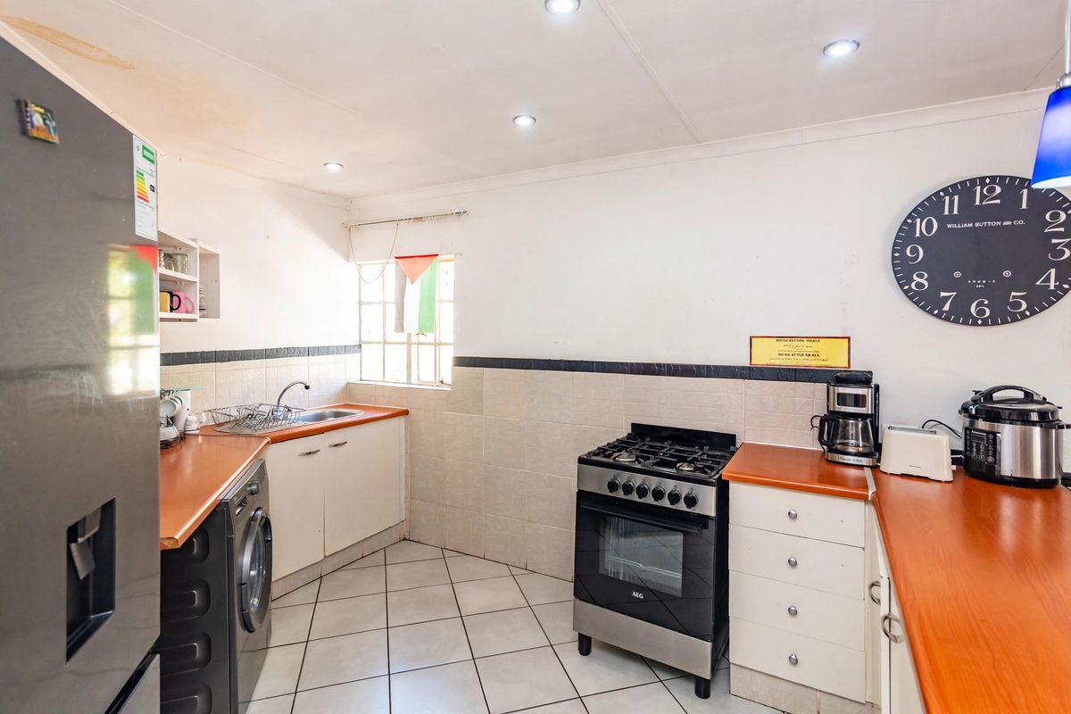 A functional kitchen featuring built-in cabinetry, laminate countertops, a gas stove with oven, and tiled flooring with a tiled backsplash.