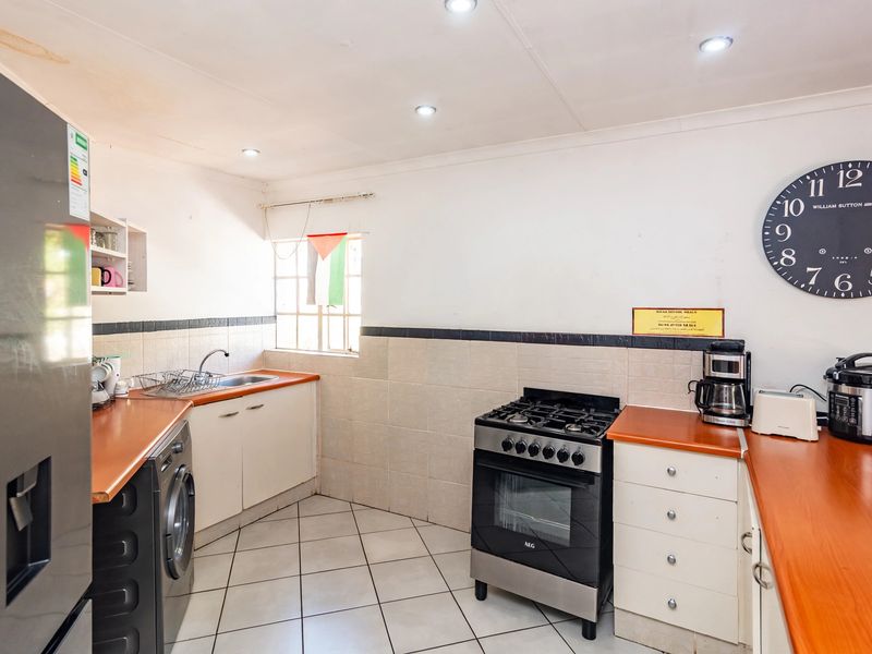 A functional kitchen featuring built-in cabinetry, laminate countertops, a gas stove with oven, and tiled flooring with a tiled backsplash.