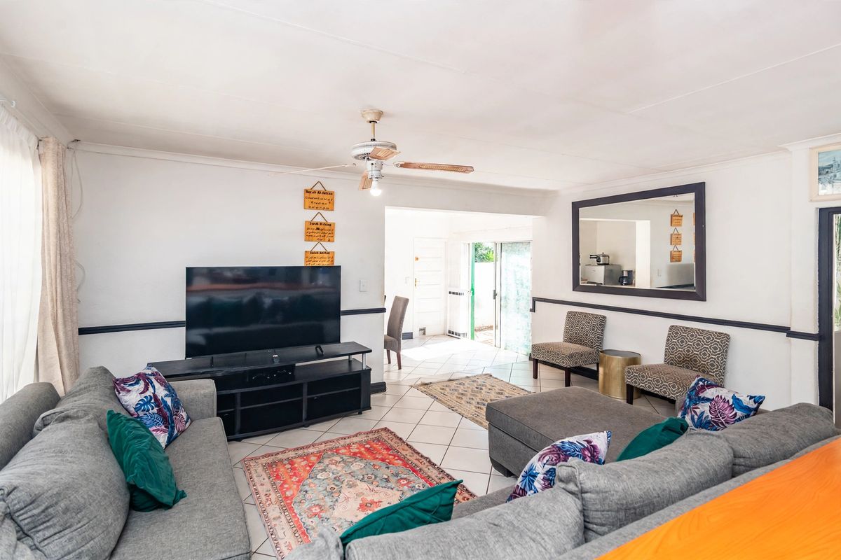 A spacious living room featuring tiled flooring, a ceiling fan, and chair rail molding, with an open flow leading to the rear entrance.