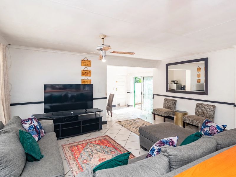 A spacious living room featuring tiled flooring, a ceiling fan, and chair rail molding, with an open flow leading to the rear entrance.