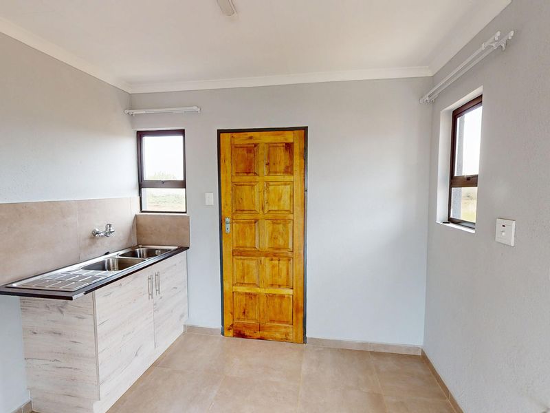 A clean and functional scullery area featuring a stainless steel double sink, laminate cabinetry, tiled splashback, and direct access via a wooden door.