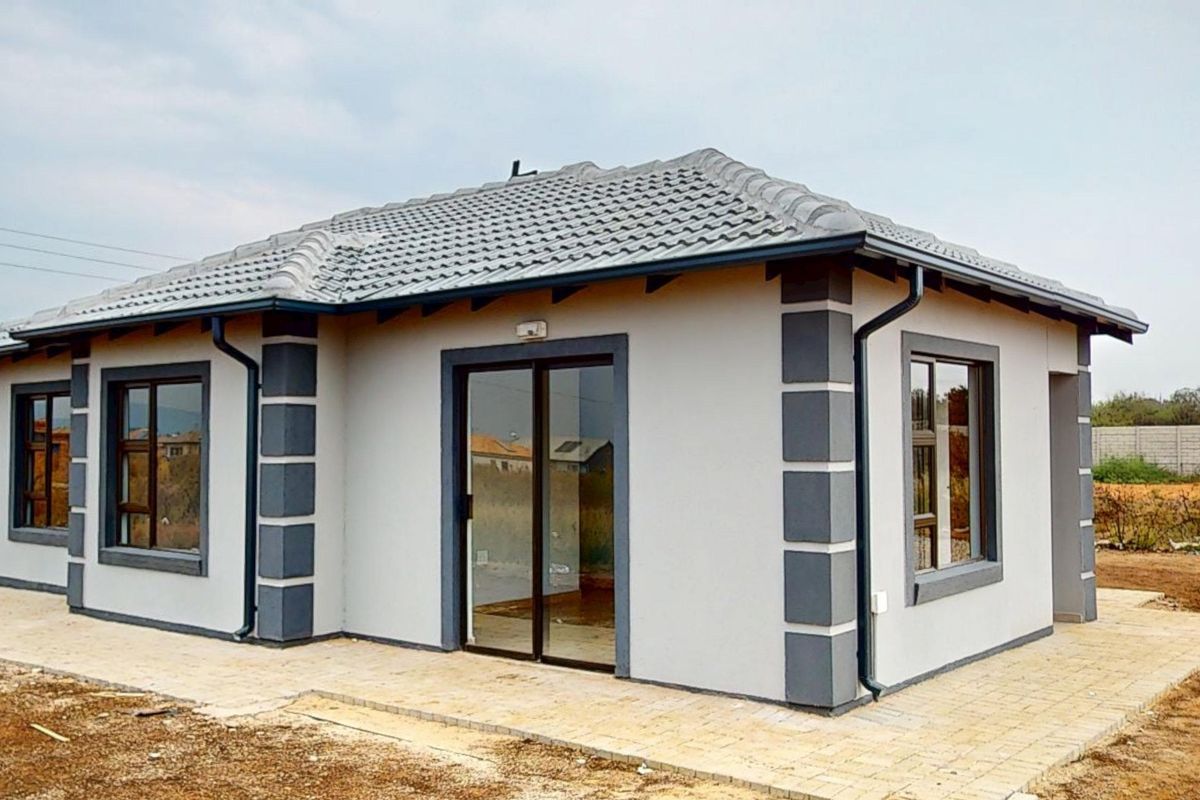 A modern single-story house exterior featuring a tiled roof, grey and white facade, aluminium window frames, and a paved patio area.