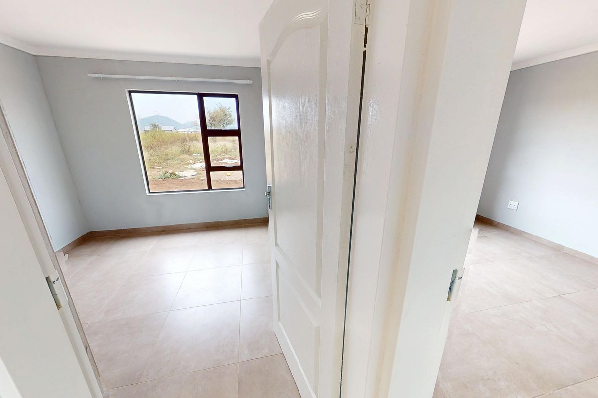 A bright, empty bedroom featuring neutral tiled flooring and a large window with views of the surrounding landscape.