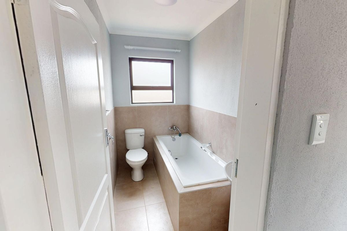 A clean, functional bathroom featuring a built-in bathtub, toilet, and neutral tiled finishes, offering a simple and well-maintained space.