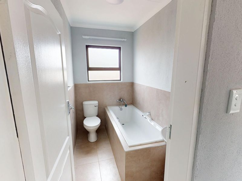 A clean, functional bathroom featuring a built-in bathtub, toilet, and neutral tiled finishes, offering a simple and well-maintained space.