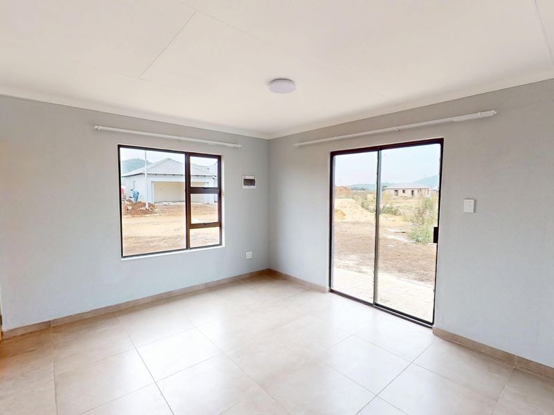 A bright, empty living room featuring neutral tiled flooring, large aluminium-framed windows, and a sliding glass door providing access to the exterior.