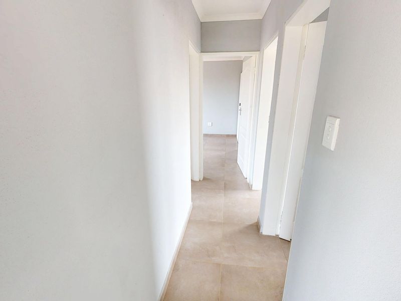 A clean, neutral-toned hallway featuring tiled flooring and multiple doorways leading to adjacent rooms.